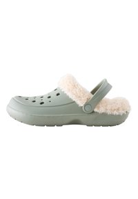 Gröna träskor med en fluffig beige krage, gjorda av mjuk plast, med ventilationshål och en rem baktill för en säker passform.