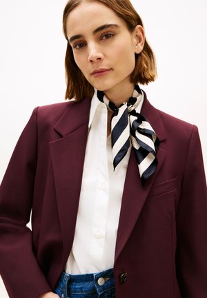 Bordowa marynarka z klapami z wycięciem, noszona na białej koszuli zapinanej na guziki, zestawiona z granatowo-białym, jedwabnym szalem w paski oraz niebieskimi dżinsami.