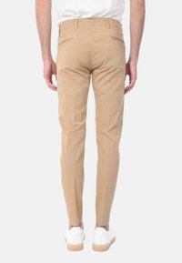 Chinos beige in cotone con una vestibilità slim. Presentano due tasche posteriori e dettagli di cucitura discreti, abbinati a sneakers bianche.