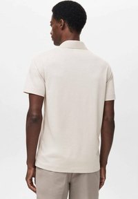Camisa polo de color beige claro, hecha de una tela suave, con un cuello clásico y mangas cortas. Diseño simple sin patrones o acentos visibles.