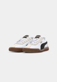 Hvide og sorte sneakers med en overdel i ruskind, gummisål og snøresystem. Har PUMA-branding på tungen og siden.