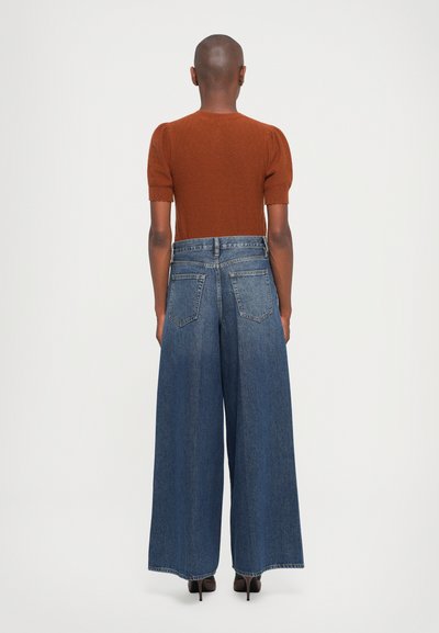 Top a maglietta a maniche corte marrone in maglia abbinato a jeans in denim blue a gamba larga con design a cinque tasche e cuciture in vista. Tessuto con una consistenza liscia.