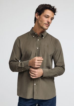 Chemise à boutons verte olive avec une coupe ajustée, dotée d'un petit logo brodé, d'un col boutonné et de manches longues. Texture du tissu douce.