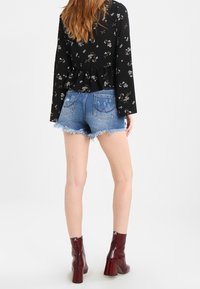 Blusa nera a maniche lunghe con motivo floreale, indossata sopra dei pantaloni shorts in denim chiaro sfilacciato, abbinata a stivaletti col tacco borgogna.