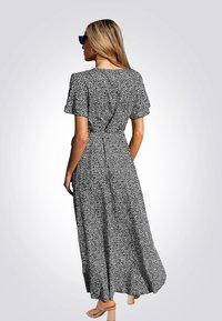 Zwart-wit gestreepte maxi-jurk met korte mouwen, aangesloten taille en vloeiende rok. Model draagt beige blokhak-sandalen.