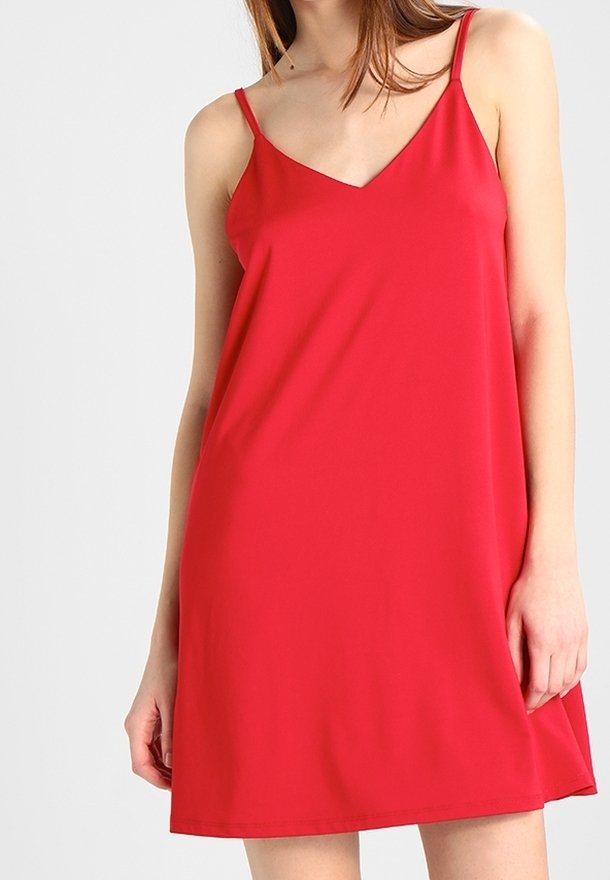 Femme portant une robe rouge sans manches avec des bretelles fines et un décolleté en V sur un fond clair uni.