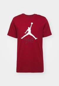 Czerwona bawełniana koszulka z białym logo Jumpman i słowem „Flight” w kolorze szarym. Klasyczny okrągły dekolt i krótkie rękawy.