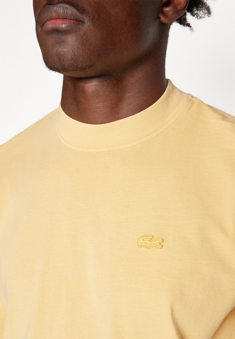 Żółta bawełniana koszulka z okrągłym dekoltem, z małym haftowanym logo na lewej piersi. Miękka tekstura i luźny krój.