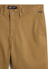 Pantalon chino couleur fauve en tissu de coton, avec deux poches latérales, une fermeture à boutons à l'avant, et une étiquette portant l'inscription "VANS AUTHENTIC CHINO".