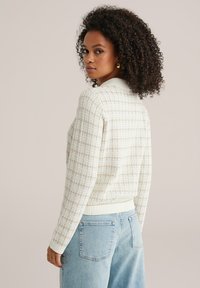 Krémový sveter s vafľovým vzorom, s rebrovaným golierom a manžetami, s voľným strihom a mierne skráteným dizajnom, v kombinácii so svetlomodrými rifľami.