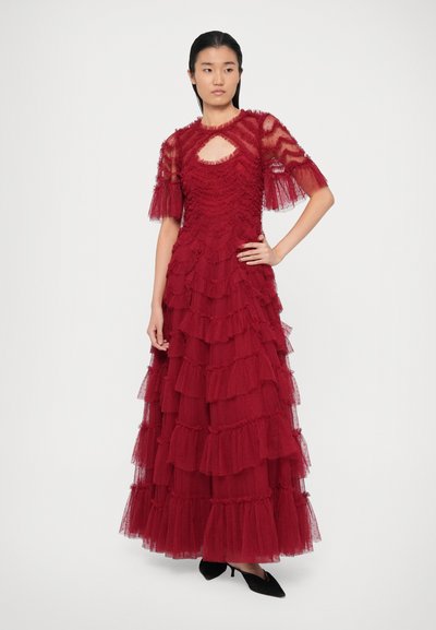 Burgundi tulle suknelė su sluoksniuotais raukiniais, trumpomis rankovėmis ir raktu formos iškirpte. Juodi smailūs bateliai puikiai papildo aprangą.