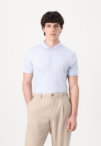 Light blue polo shirt with a collar and two buttons, paired with beige, textured trousers with a single button closure at the waist.