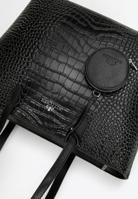 Czarna torba tote z tłoczonym wzorem krokodyla, z płaskimi ramiączkami, wyposażona w okrągłą odczepianą koronkę oraz szczegół z logo w kolorze srebrnym. Gładkie i teksturowane powierzchnie.