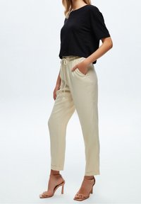 T-shirt noir court à manches courtes associé à un pantalon beige clair à cordon de serrage. Des sandales à talons hauts couleur camel complètent la tenue.