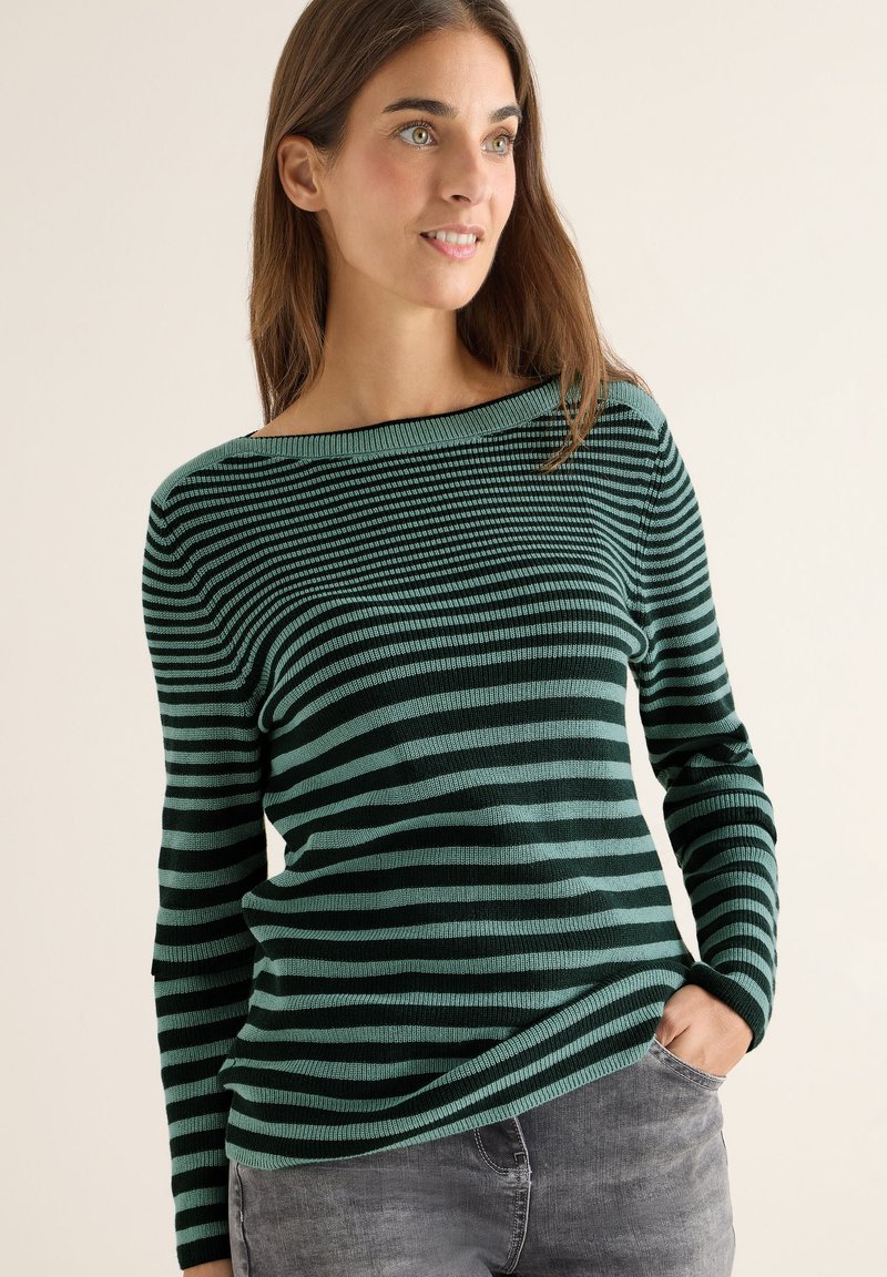Maglione a maniche lunghe verde e nero a righe con scollo a barca, texture a costine e vestibilità rilassata, abbinato a jeans grigi.