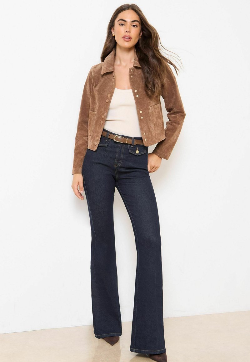 Brun mockalädercroppad jacka med knappstängning och två frontfickor, tillsammans med mörkblå utsvängda jeans och en beige topp.