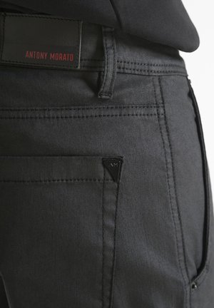 Primer plano de un bolsillo de pantalón negro con costuras cosidas, un lazo para cinturón y una etiqueta rectangular que dice "ANTONY MORATO" en letras rojas.