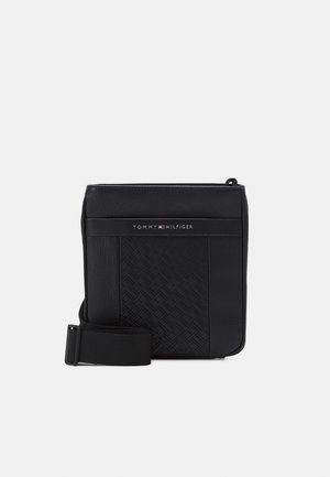 Sac bandoulière noir avec motif embossé, sangle réglable, fermeture éclair sur le dessus et logo Tommy Hilfiger sur le panneau avant.