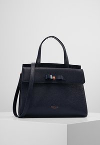 Granatowa torebka o strukturalnym kształcie, wykonana z teksturowanej skóry, z przednim klapem, akcentem w postaci kokardy oraz podwójnymi uchwytami do noszenia z odpinanym paskiem.