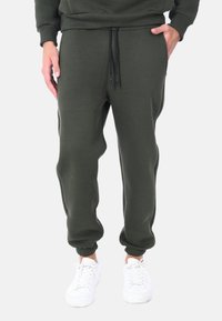 Pantaloni jogger verde scuro realizzati in tessuto morbido, con vita elastica e cordini regolabili, polsini aderenti e abbinati a sneakers bianche.