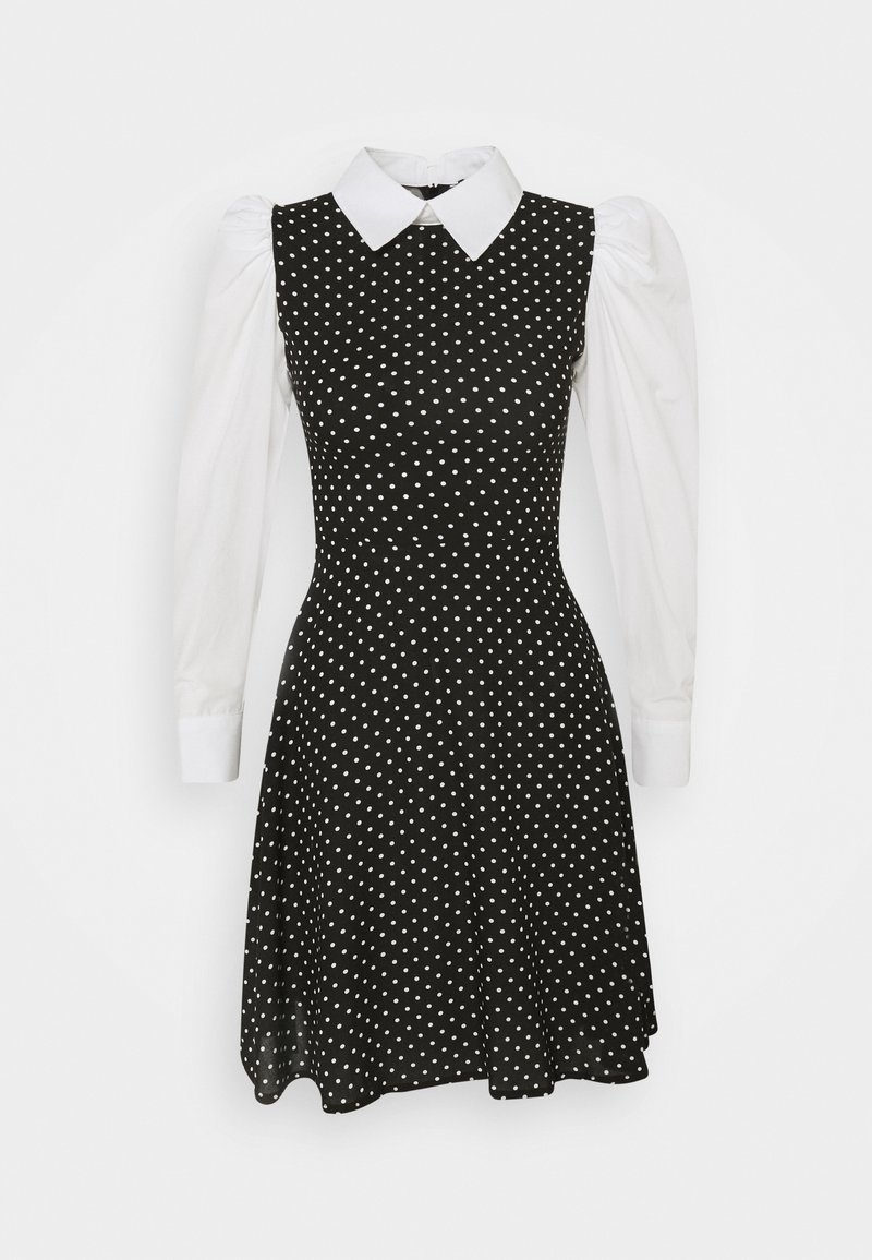 Robe noire à pois blancs, dotée d'un corsage structuré, de manches bouffantes blanches et d'un col classique, s'évasant délicatement au niveau de la jupe.
