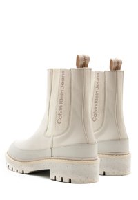 Stivali Chelsea bianchi in pelle liscia con pannelli elastici laterali e linguette beige. Suola in gomma spessa maculata per trazione e supporto.