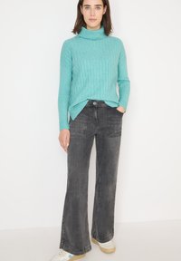 Pull en col roulé turquoise avec texture à côtes, associé à un jean flare gris taille haute et des baskets blanches avec des accents bleus.