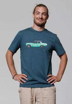 Teal t-shirt met korte mouwen, voorzien van een grafiek van een lichtblauwe vintage auto met een surfplank op het dak, gecombineerd met beige broek.