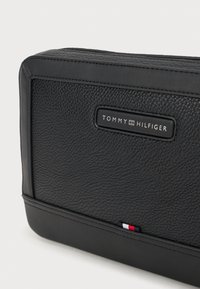 Must värviline nahk piraat, millel on ristkülikukujuline kuju. Esile tõstetud "TOMMY HILFIGER" silt ja väike punane, valge ja sinine aksent.