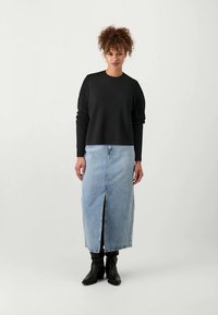 Črna dolga majica z dolgimi rokavi v kombinaciji z svetlo modrim denim krilom, ki ima razporek spredaj. Črne gležnjarje dopolnjujejo obleko.