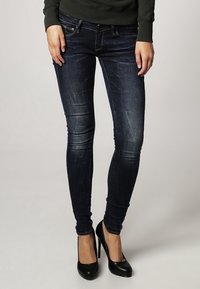 Mörkblå skinny jeans med en urtvättad finish och subtila slitningar, i kombination med svarta högklackade skor. Slät denimtextur.