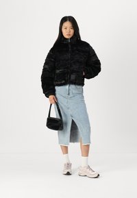 Jachetă scurtă din blană sintetică neagră cu guler înalt, fustă din denim albastru deschis cu fanta în față, geantă neagră și adidași roz deschis.