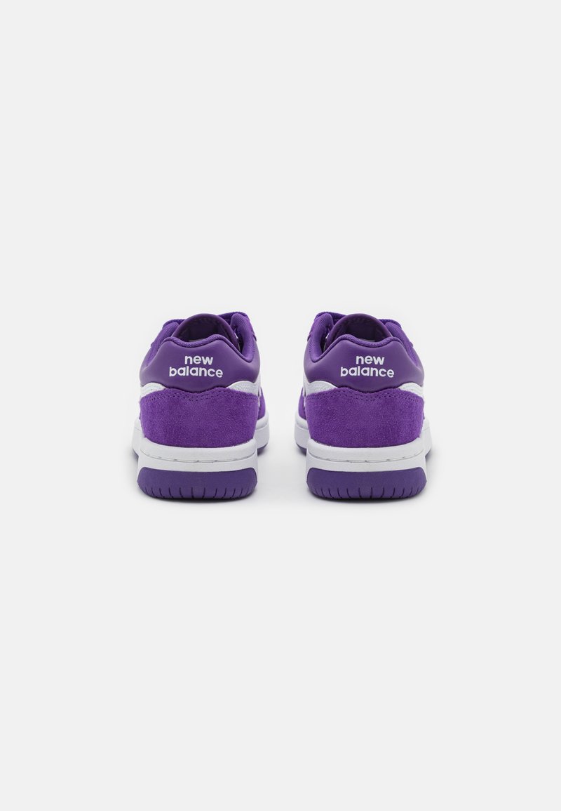 Baskets en suede violet avec des accents blancs. Présente un logo bien visible sur le talon, une semelle intermédiaire rembourrée et une semelle extérieure en caoutchouc texturée.