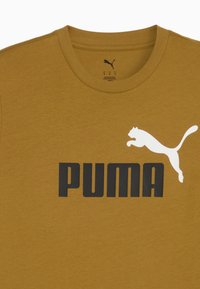Camiseta de color mostaza de Puma con el texto "PUMA" en negro y el logo de Puma saltando en blanco en el frente.