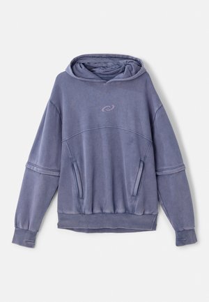 Hoodie violet en tissu doux, avec une capuche à cordon, des poignets côtelés, des poches avant et un logo circulaire sur la poitrine.