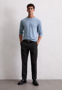 Hellblaues langärmliges Sweatshirt, schwarze Hose, schwarze Schuhe; taillierter Schnitt mit glatter Textur, keine sichtbaren Muster oder Logos.