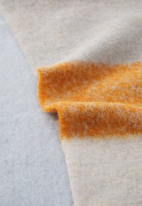 Tissu en laine présentant des nuances douces de gris et de crème avec une bande orange vive. Surface texturée offrant une sensation chaleureuse et confortable.