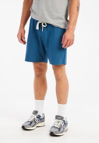 Blå shorts med en struktureret overflade og en elastisk talje, med snoretræk. Parret med grå træningssko og hvide sokker.