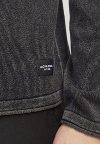 Grå teksturert hettegenser med logo-patch, kontrasterende sømmer og avslappet passform. Materialet ser mykt og slitesterkt ut.