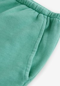 Joggers turcoaz din bumbac, cu talie elastică, având un finisaj texturat și buzunare laterale. Materialul pare moale și ușor.