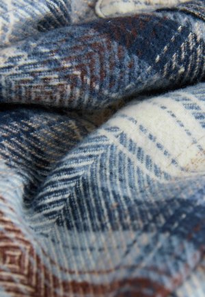 Wolldecke mit einem blau- und cremefarbenen Fischgrätmuster und braunen Akzenten. Weiche Textur, gefaltet, um die kunstvollen Webdetails hervorzuheben.