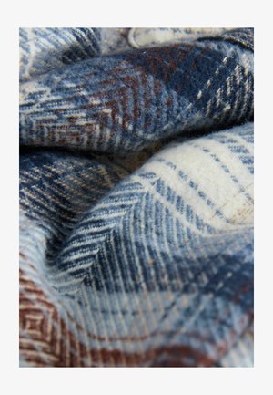 Gyapjú takaró kék és krém színű halszálka mintával, barna részletekkel. Puha textúra, meghajtva, hogy kiemelje a bonyolult szövési részleteket.