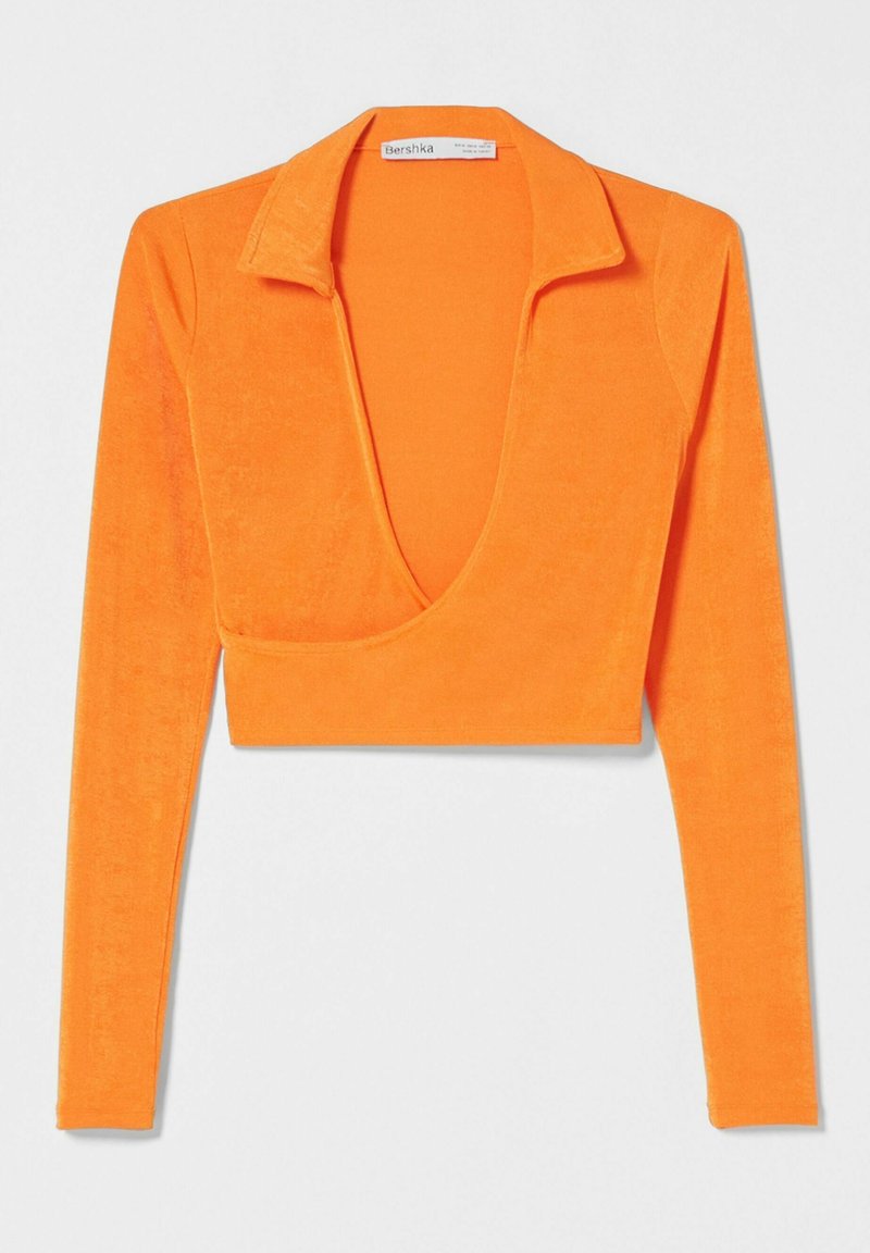 Top corto de manga larga en color naranja con un escote en V profundo y una tela texturizada. Cuenta con un cuello con muesca y una silueta ajustada.