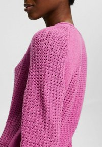Maglione all'uncinetto fucsia brillante, caratterizzato da una trama a rete aperta, maniche lunghe e una vestibilità comoda con scollo rotondo.
