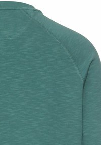 Teal long-sleeve top made from a textured, breathable fabric. Features a rounded neckline and raglan sleeves with subtle color variations.