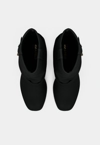 Mustad pahkluu saabastega, millel on sile tekstuur, ümmargune nina, kihiline disain ja külgmine lukk. Lukule on lisatud kuldsed detailid.