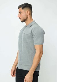 Polo gris à manches courtes en tissu tricoté texturé, avec une patte de boutonnage, une poche poitrine et des bords côtelés sur les manches et l'ourlet.