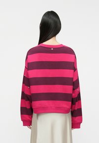 Sweatshirt às riscas rosa e burgundy com gola redonda, corte descontraído e tachas prateadas decorativas nas mangas. A parte de trás apresenta um pequeno detalhe em forma de coração.