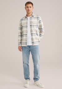 Rutig skjorta i kräm, blått och brunt; två bröstfickor. I kombination med ljusblå jeans och vita sneakers. Enkelt design.