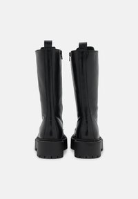 Des bottes noires en cuir, montant jusqu'au genou, avec une finition lisse, des zips latéraux et de solides semelles en caoutchouc noir texturé. Coutures renforcées visibles.